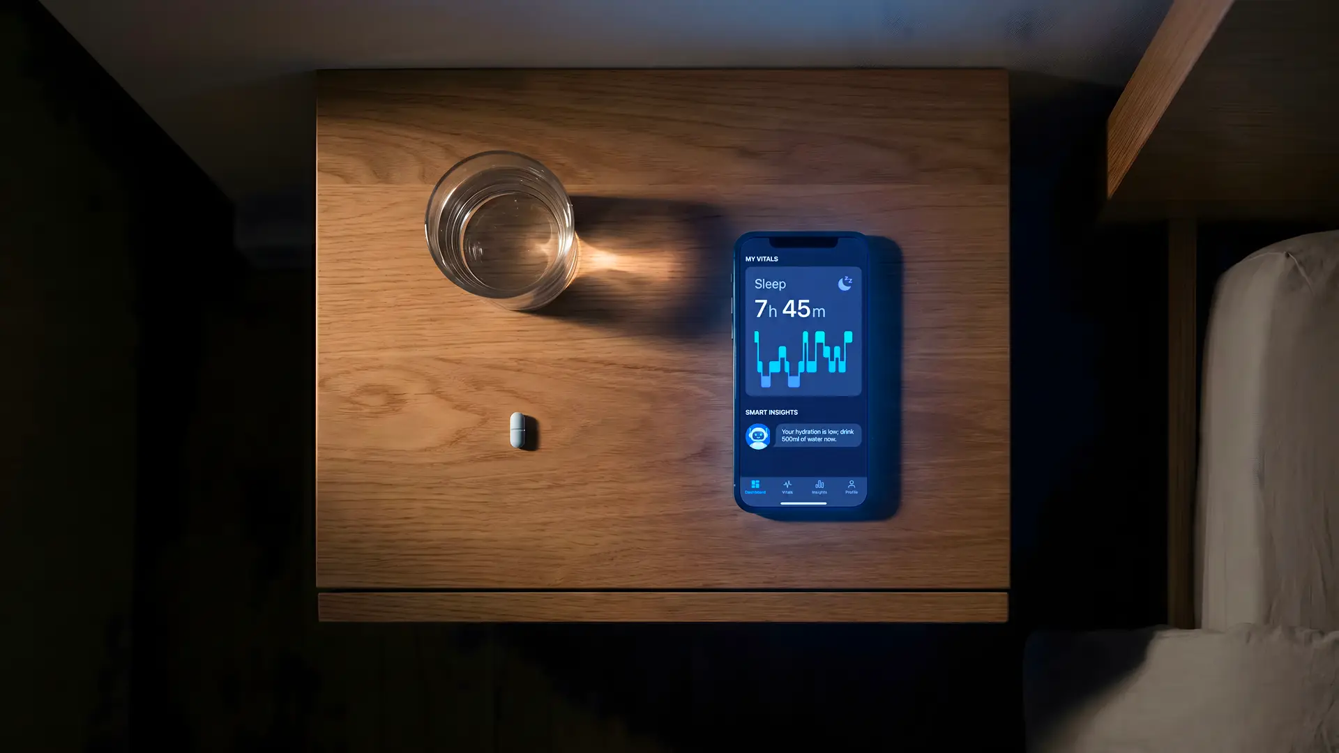 Comodino in legno visto dall'alto, di notte: bicchiere d'acqua, una compressa e uno smartphone che mostra le ore di sonno rilevate da un'app di tracking.